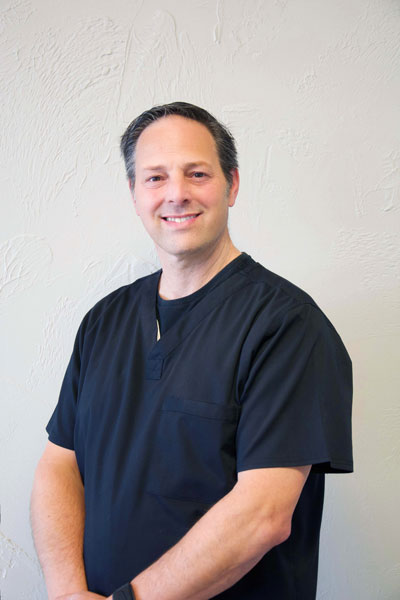 Image of a male dentist facing the camera and smiling, wearing black scrubs